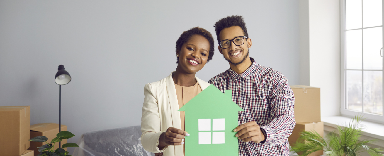 picture of a diverse, happy couple holding a silhouette of a home, inside a great room of their new home.